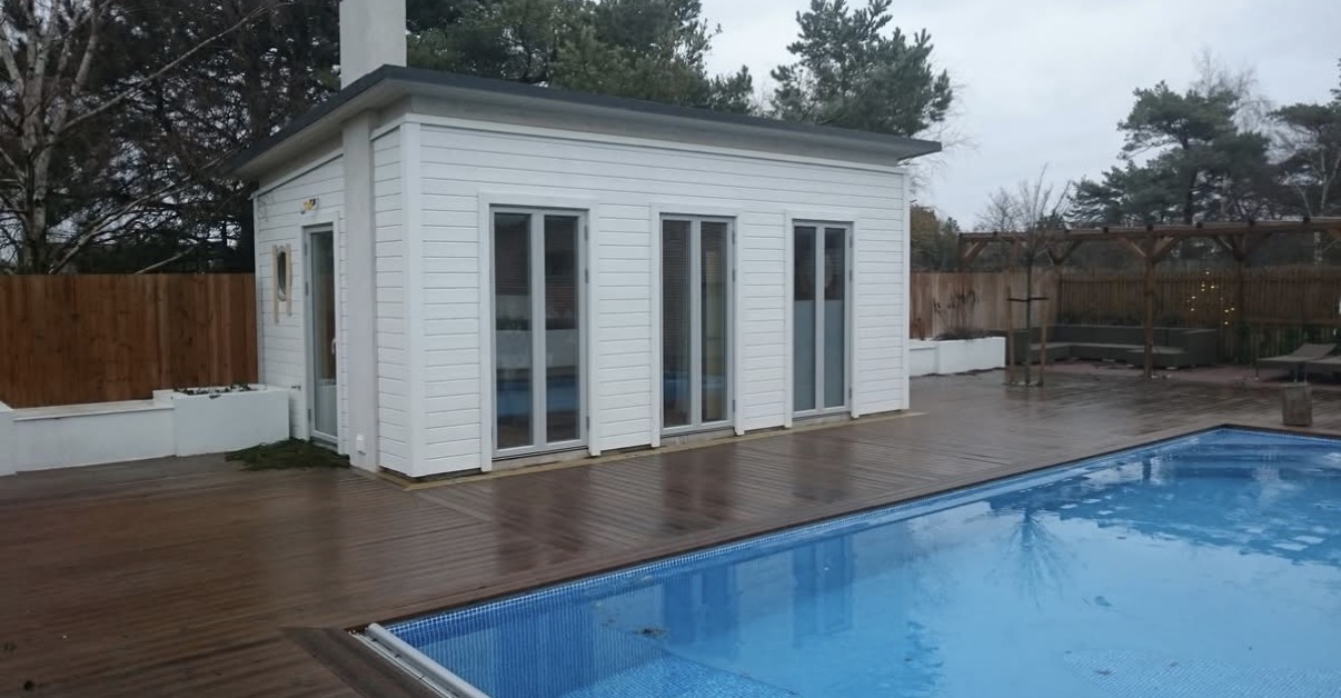 Vitt gästhus vid en pool med ett omgivande trädäck