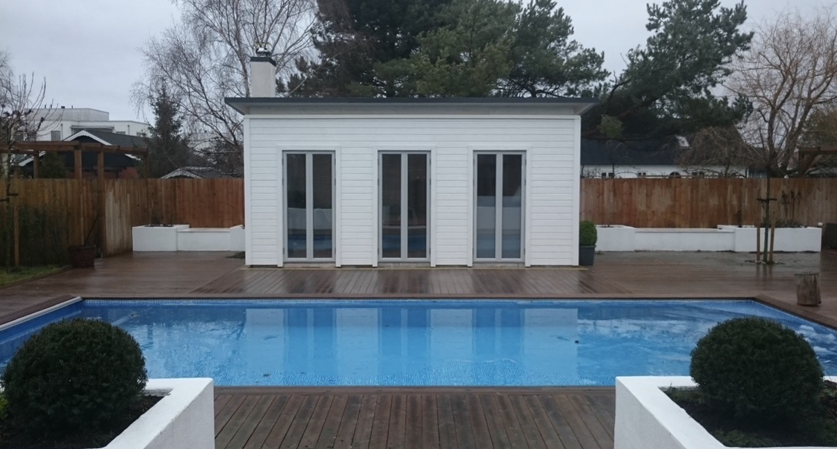 Vitt poolhus med trädäck och murade planteringar runt en pool